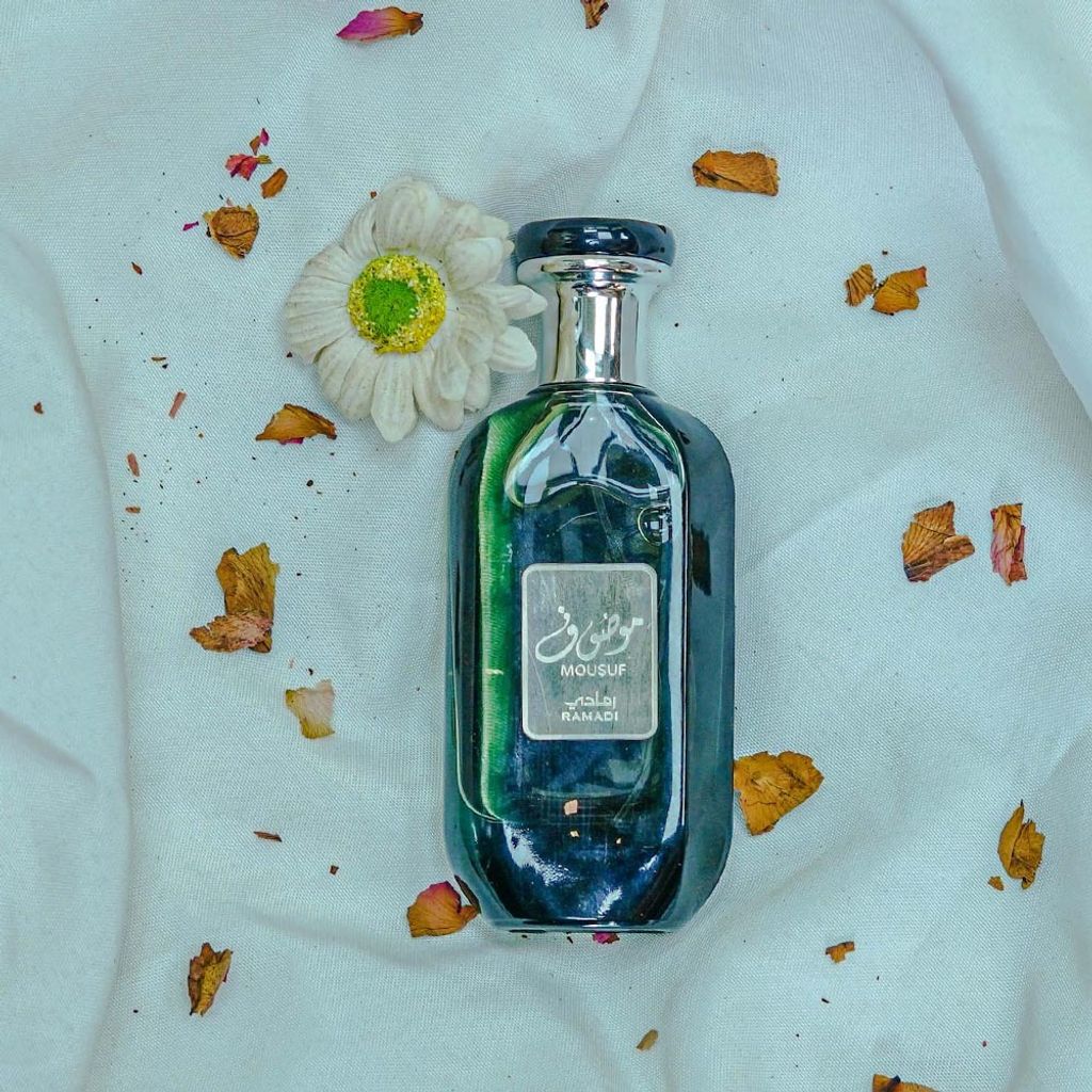 A bottle of perfume is placed on a white fabric with dried flower petals scattered around it.