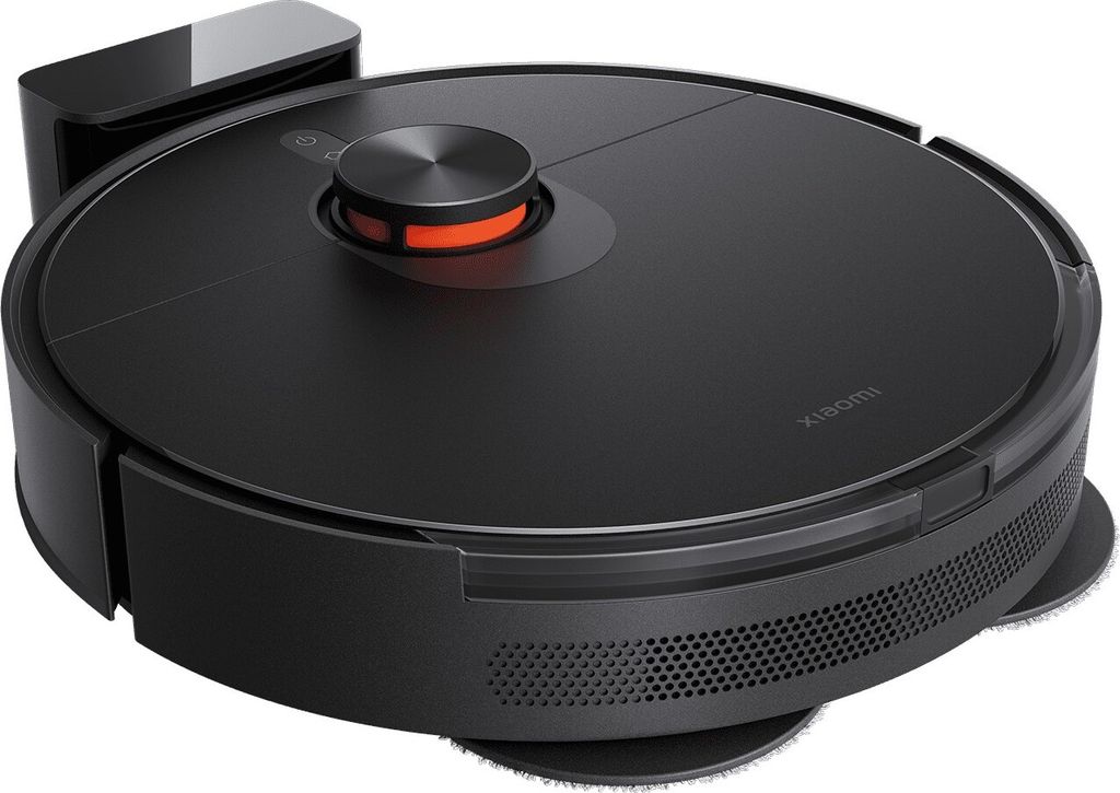 A black robot vacuum cleaner with an orange accent, shown from a slightly elevated side angle. It is positioned on a white background with its charging dock visible on the left.