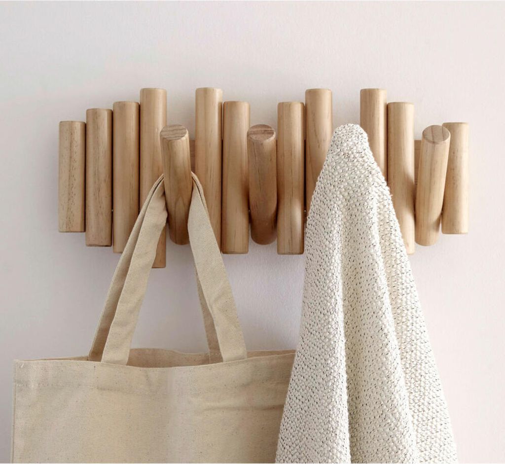 A wooden coat rack with hooks mounted on a white wall, holding a tote bag and a textured blanket.