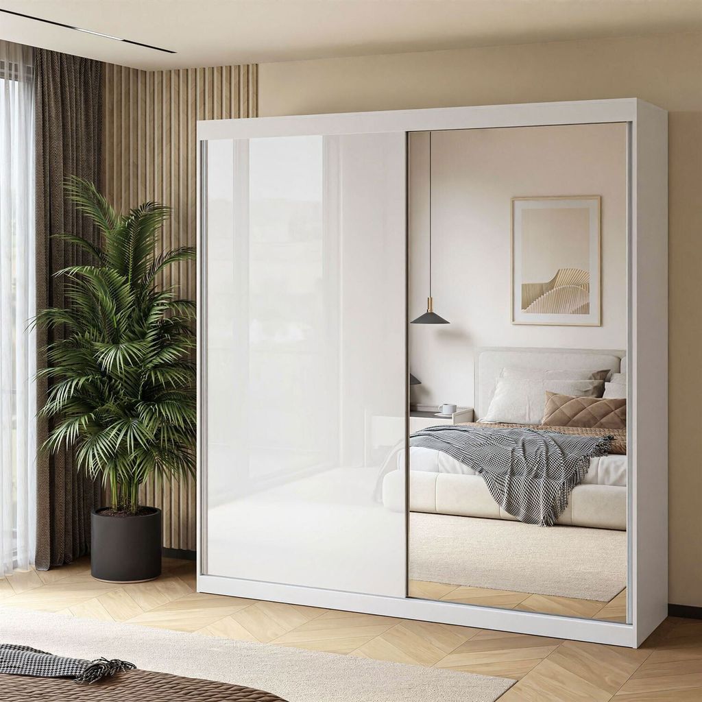 A modern bedroom with a large white sliding door wardrobe with mirrored doors, reflecting a bed and a framed picture on the wall. A large potted plant is placed next to the wardrobe.
