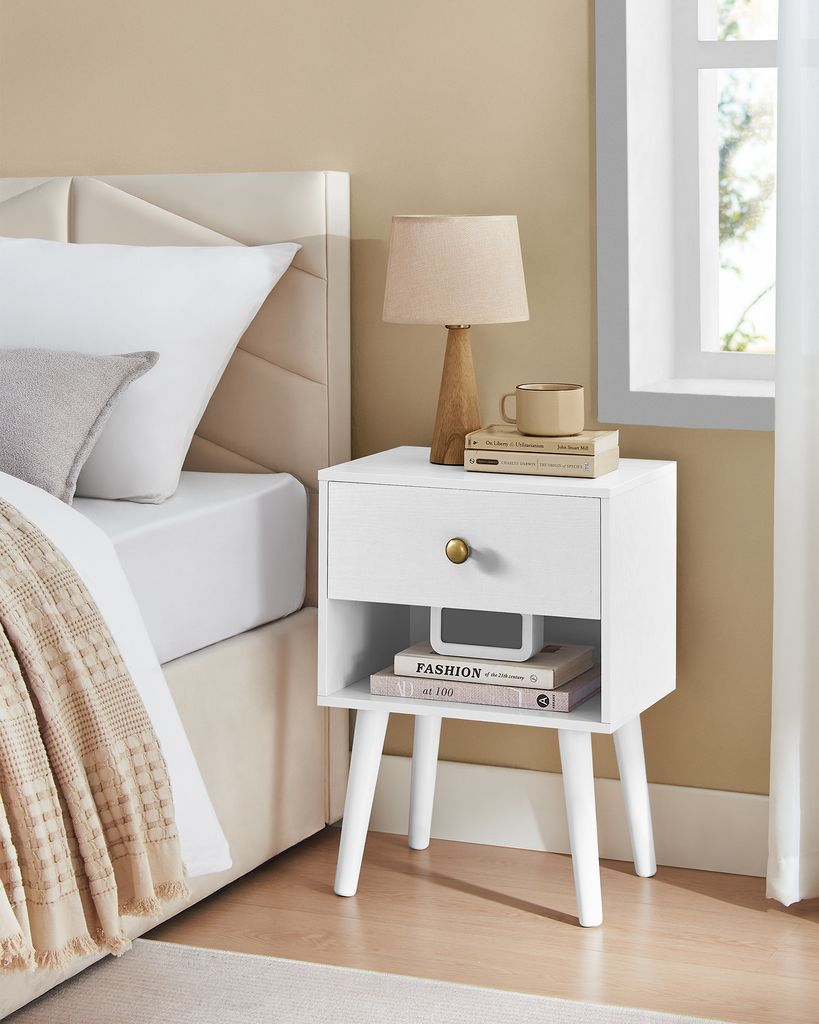 A white nightstand with a drawer and open shelf sits next to a bed.