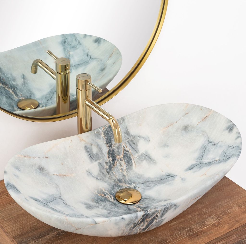 A marble sink with a gold faucet is shown in a bathroom setting, reflected in a round mirror.
