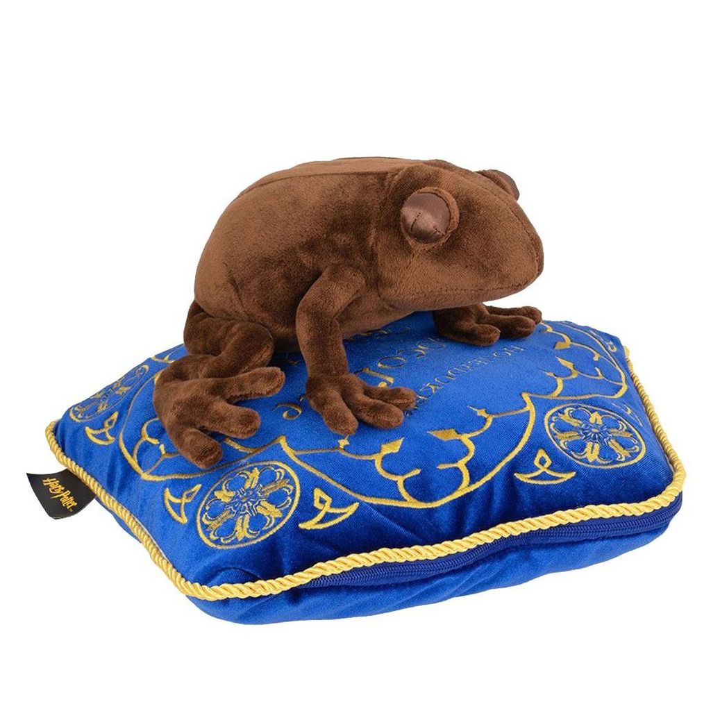A brown plush frog sits on a blue pillow with gold trim and designs.