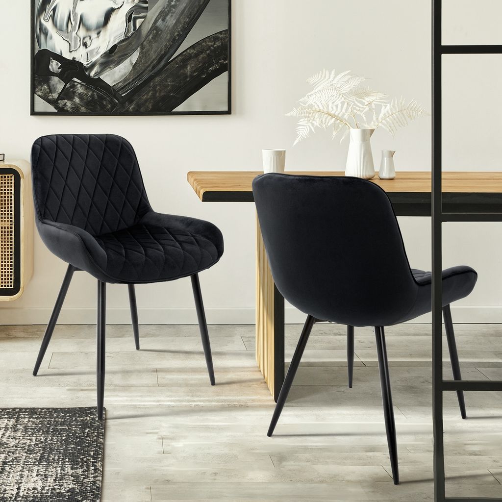 Two black velvet dining chairs are shown in a dining room setting.