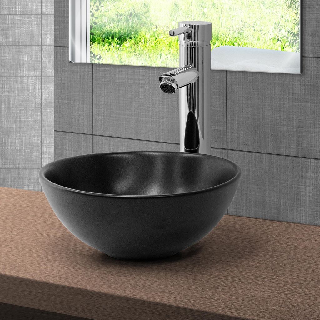 A black ceramic vessel sink with a chrome faucet is shown on a wooden countertop, with a tiled wall and a window reflecting greenery in the background.