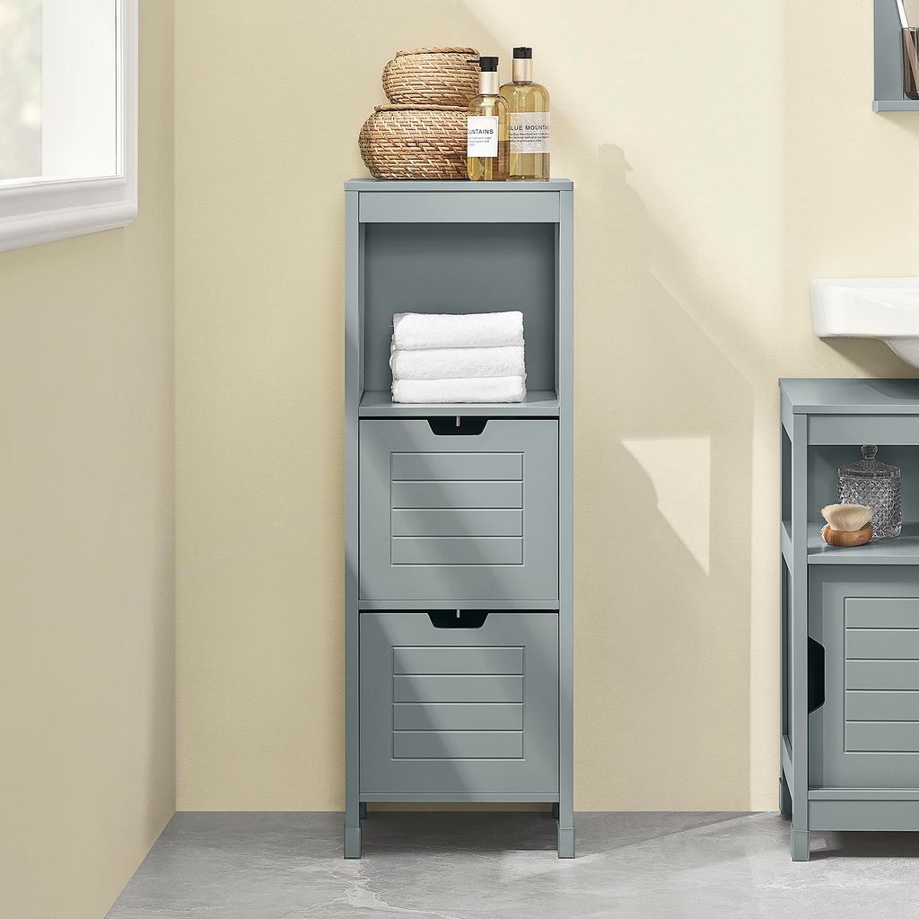 A gray wooden bathroom cabinet with two drawers and an open shelf, decorated with towels, baskets, and bottles.