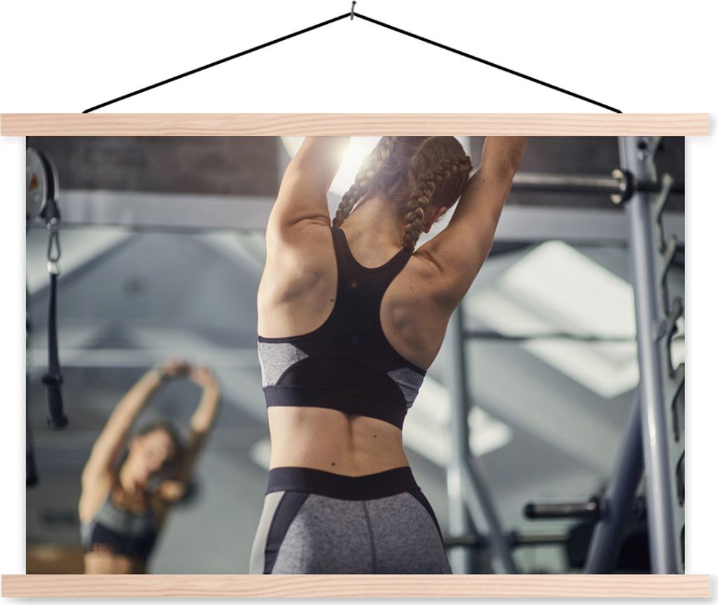 MuchoWow Textilposter Eine junge Frau dehnt sich bei einem Fitnesstraining 120x80 cm mit holzfarbenen Rahmen - Aufhängeset