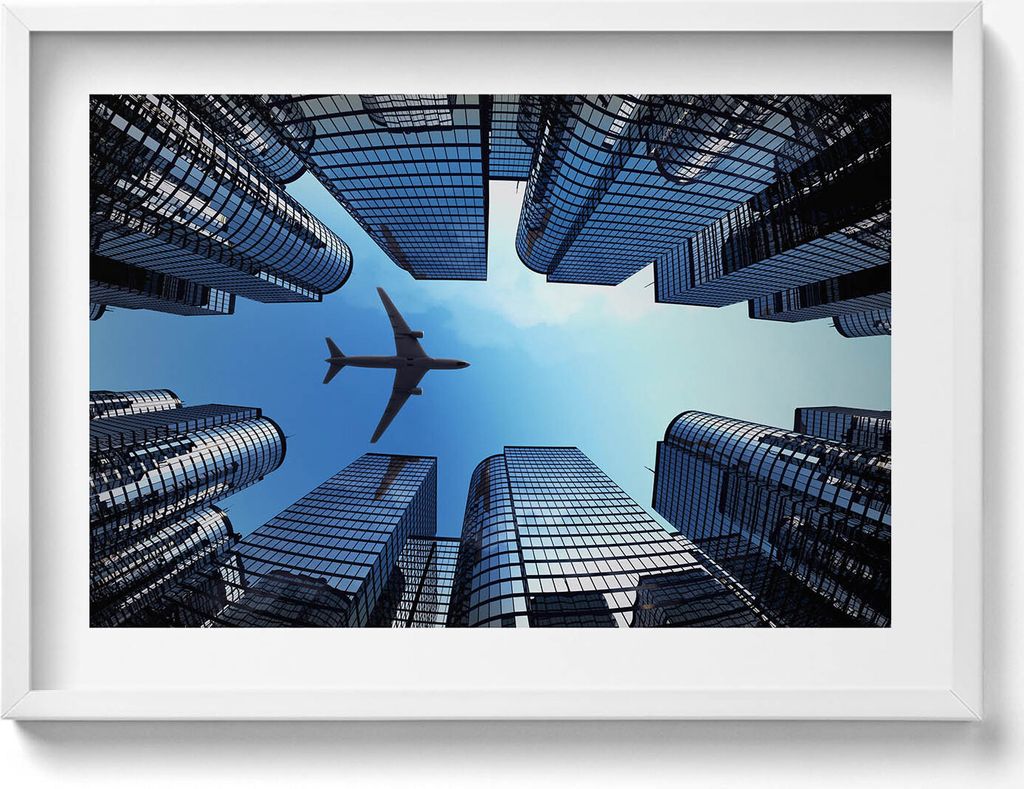Flugzeug über Gebäuden– Wandbild mit Rahmen – Gerahmtes Bild – Wanddekoration – 70x50 cm – Weiß Rahmen