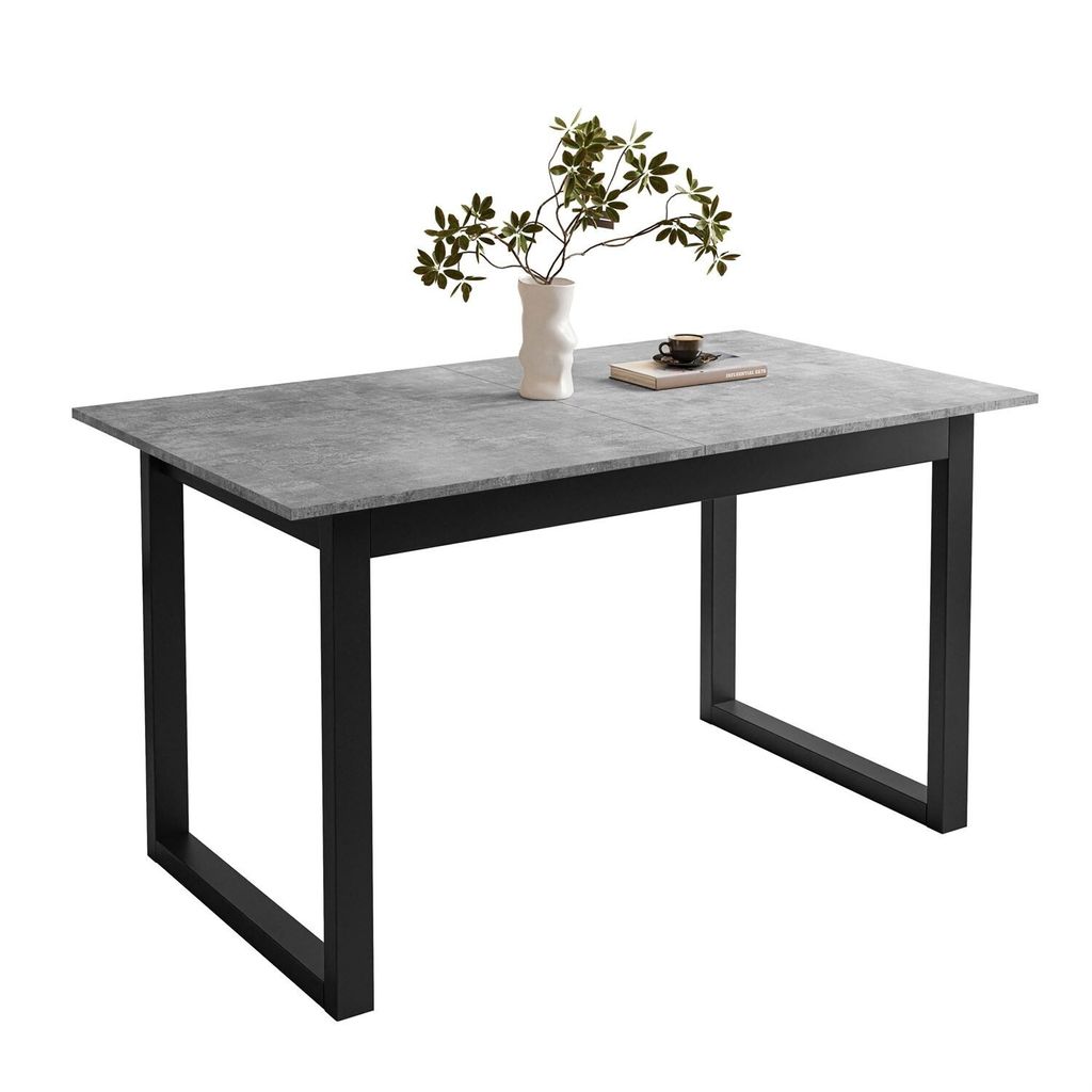 A dining table with a gray stone-like top and black metal U-shaped legs, with a vase of greenery and a book on top.