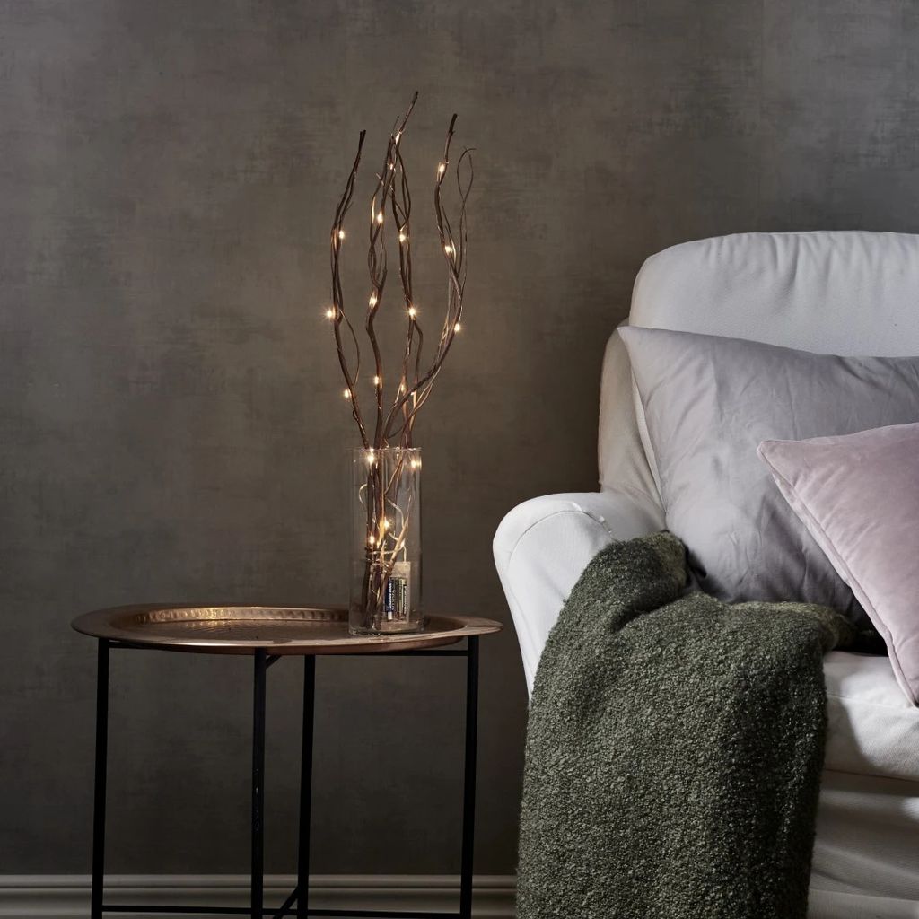 A decorative set of LED twig lights in a vase on a side table next to a sofa.