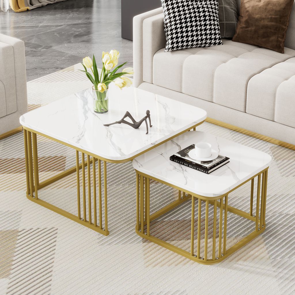 A set of two nesting square coffee tables with a white marble-look top and gold metal legs, placed in a living room setting next to a sofa.