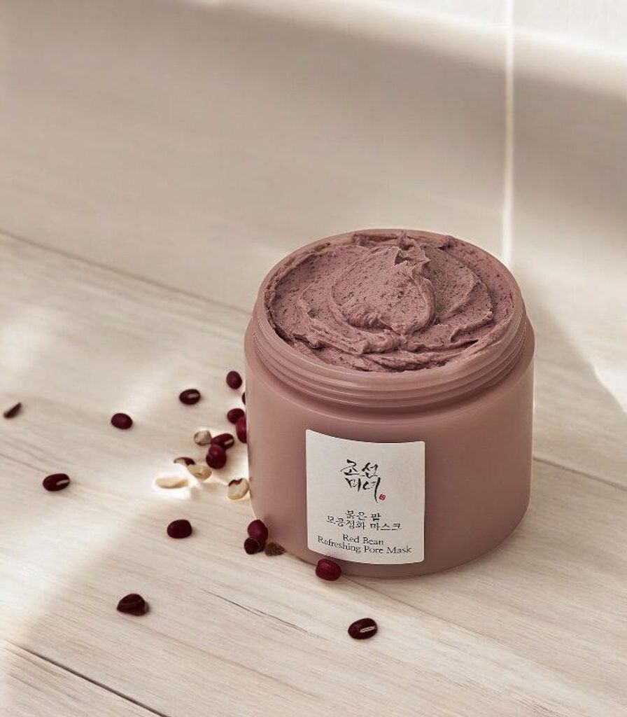 A jar of red bean refreshing pore mask is placed on a light-colored wooden surface, with scattered red beans around it.