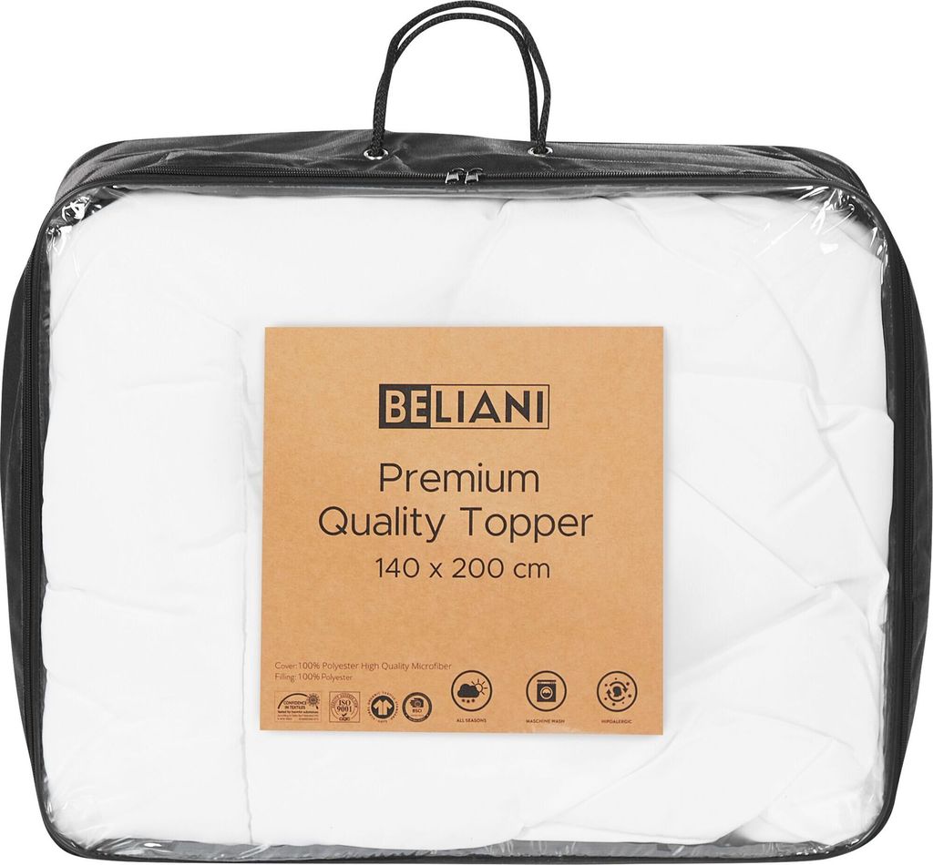 A white mattress topper is shown inside a clear plastic bag with handles, with a cardboard label attached to the front.