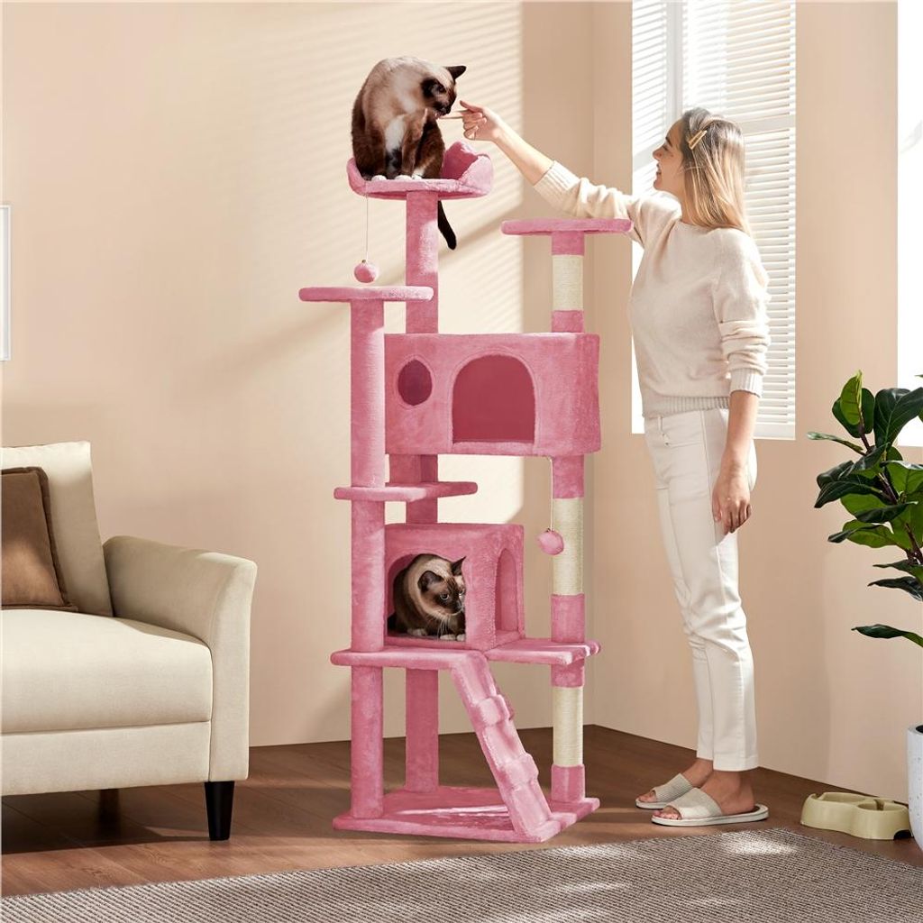 A woman is interacting with a cat on a pink cat tree in a living room.