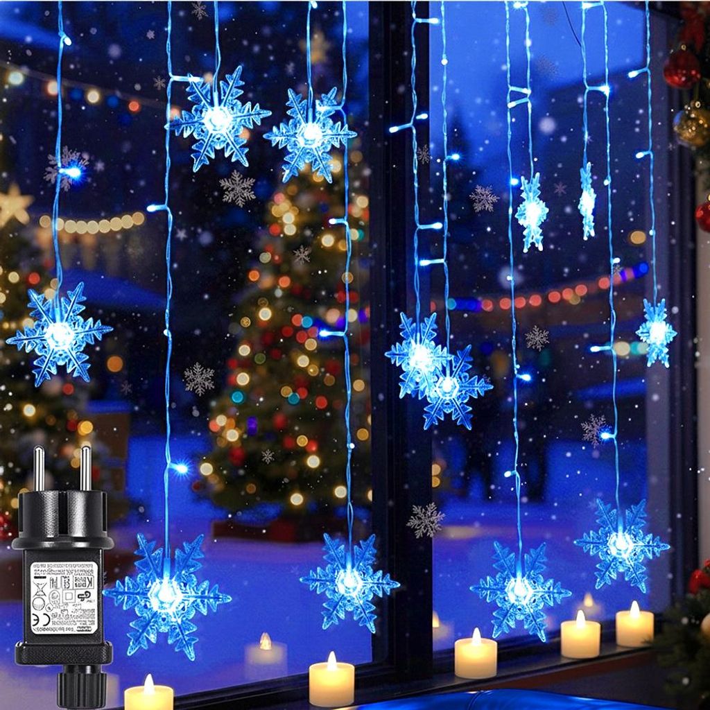 A window decorated with blue snowflake string lights, with a Christmas tree and candles visible in the background.