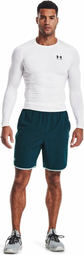 A man wearing a white long-sleeved shirt and teal shorts, standing against a white background.