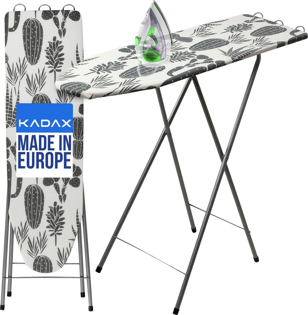 A KADAX ironing board with a cactus pattern is shown, with an iron placed on it. The ironing board is folded and standing upright next to the main ironing board. A blue label with white text is visible on the upright ironing board.
