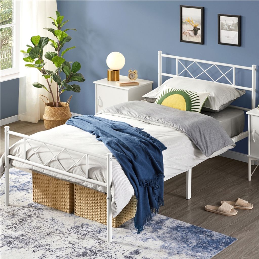 A white metal bed frame with a blue blanket and pillows, placed in a bedroom with blue walls and a rug.