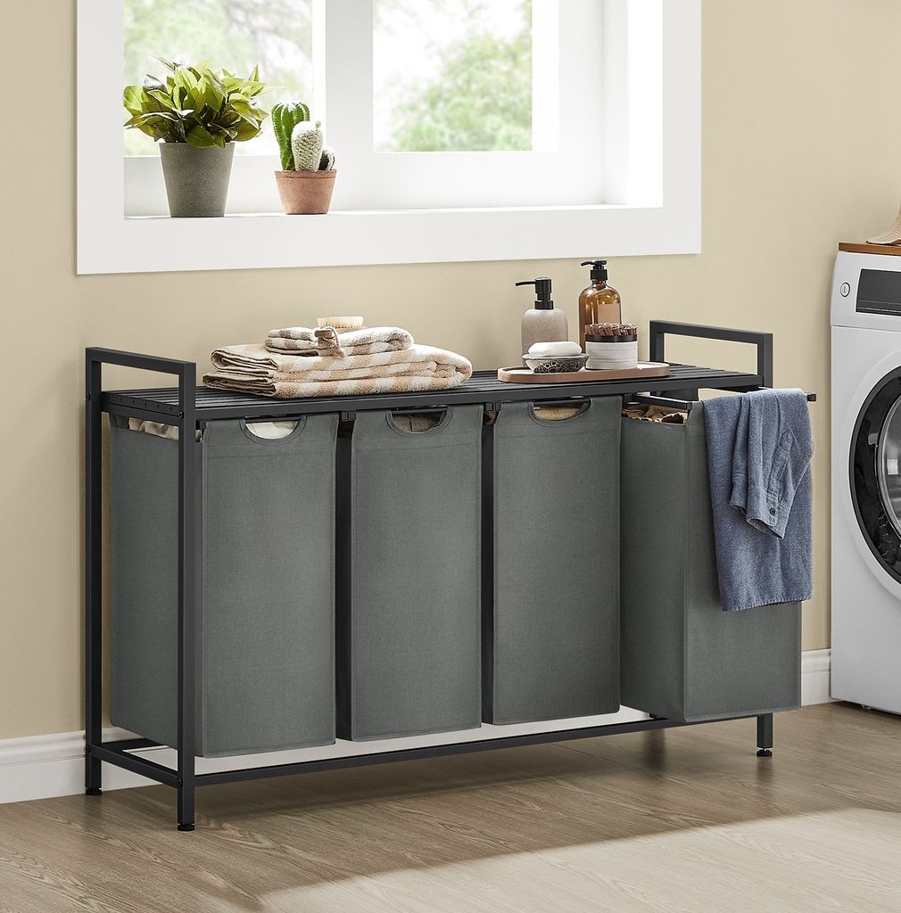 A laundry room scene with a multi-compartment laundry hamper, a washing machine, and decorative items on a shelf.