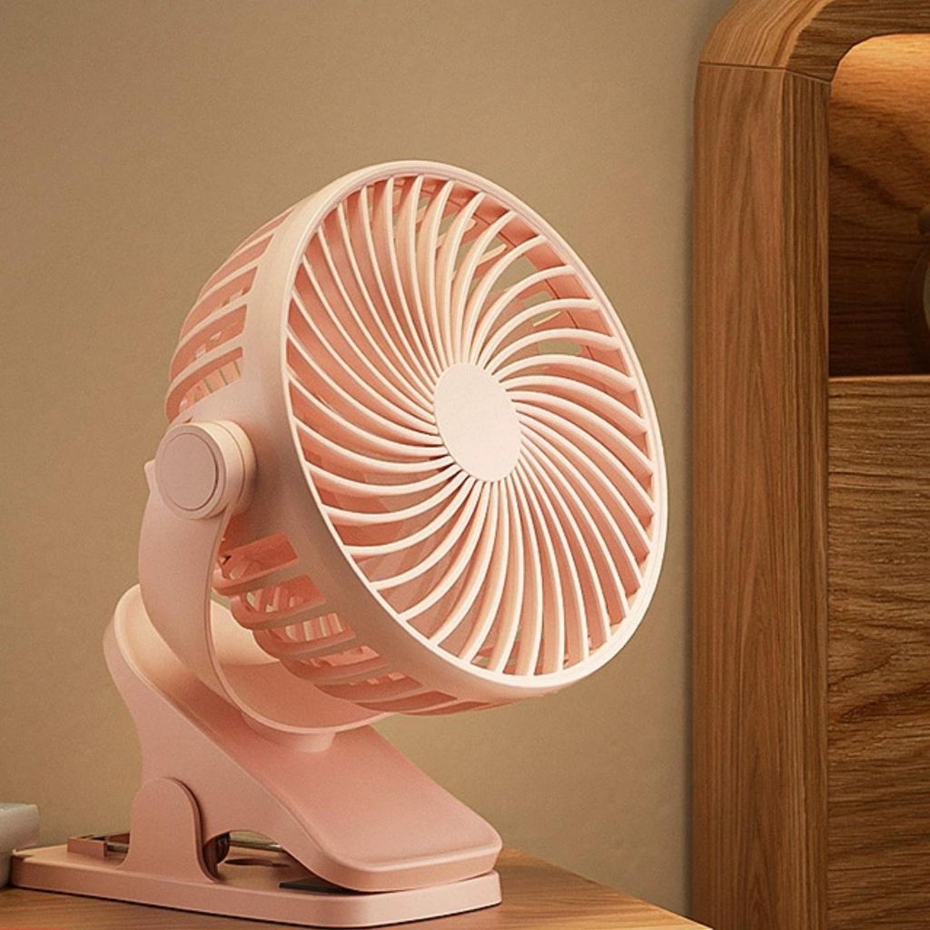 A close-up shot of a pink clip-on fan sitting on a wooden surface, next to a wooden cabinet.