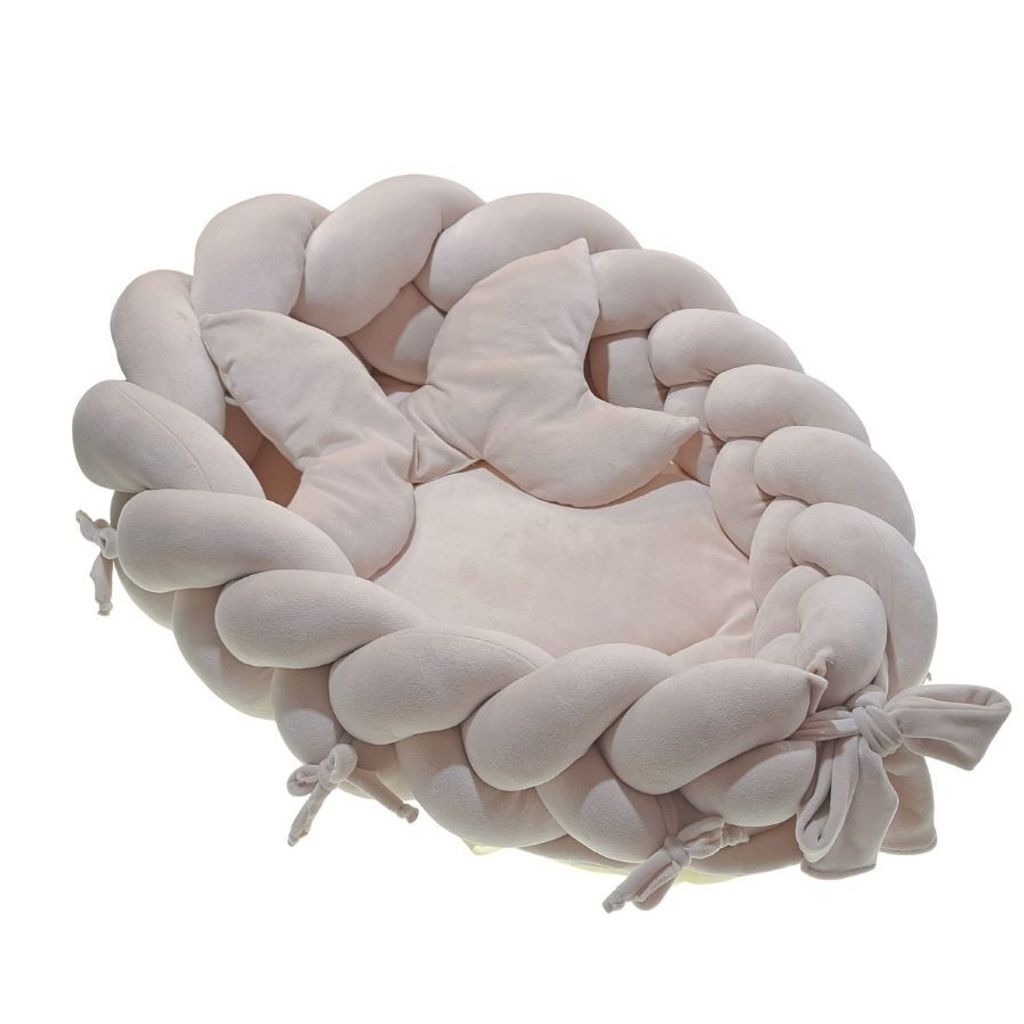 A baby nest with braided sides and a crescent-shaped pillow, presented on a white background.
