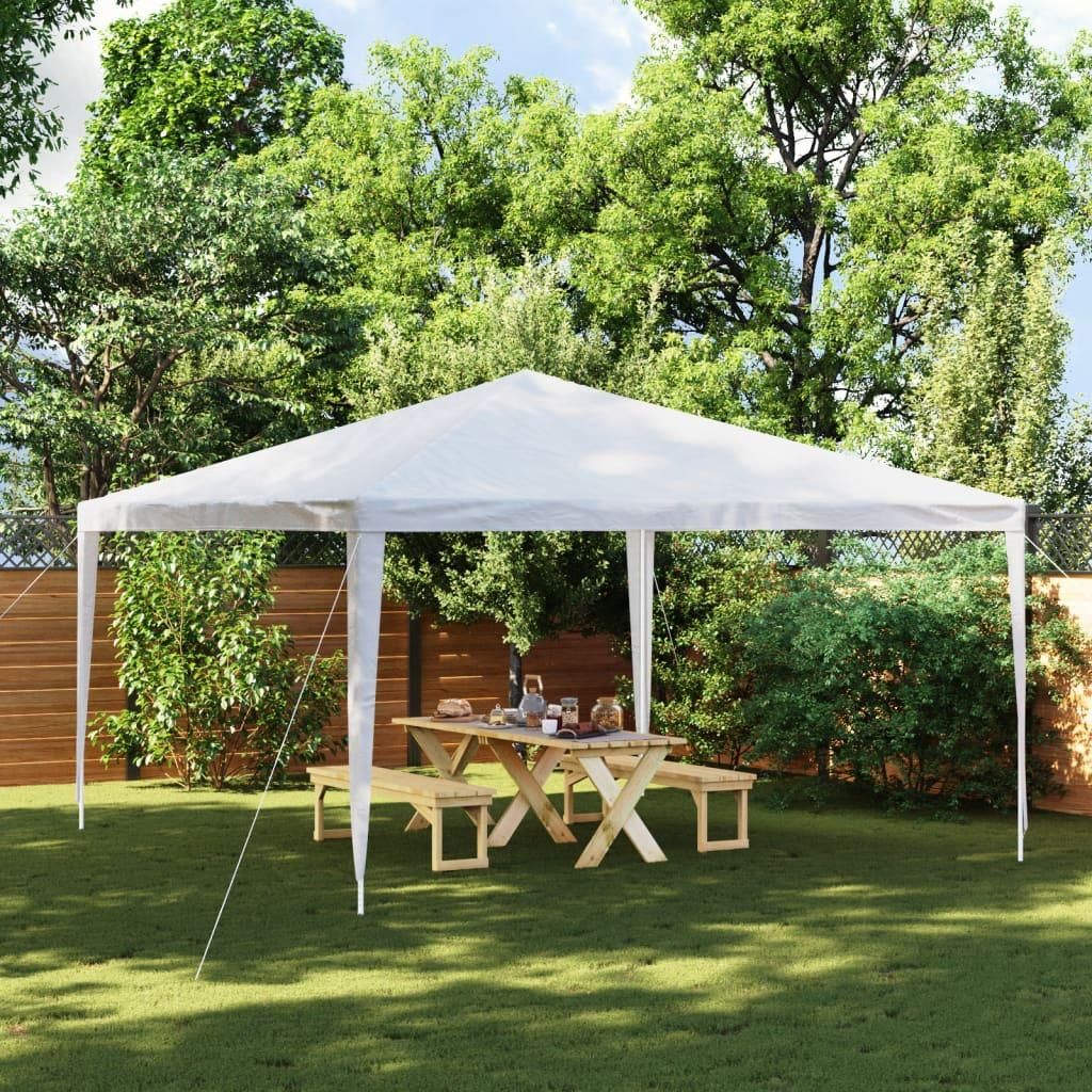 A white party tent set up in a backyard with a wooden picnic table and benches underneath.