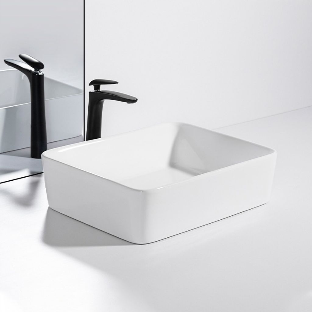A white ceramic vessel sink with a black faucet is shown on a white countertop with a mirror reflection.