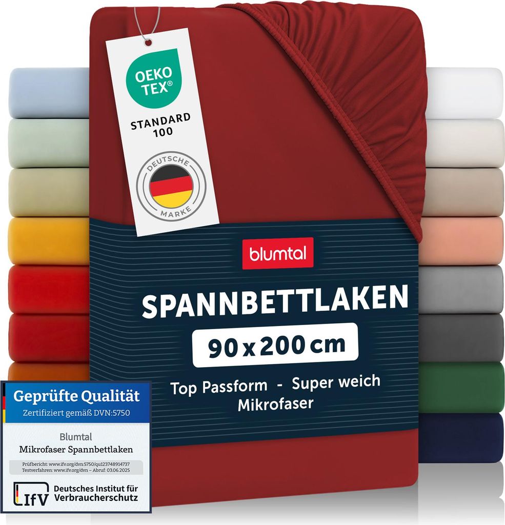 A stack of folded fitted sheets in various colors, with a red fitted sheet prominently displayed in the foreground, featuring product information and certifications.