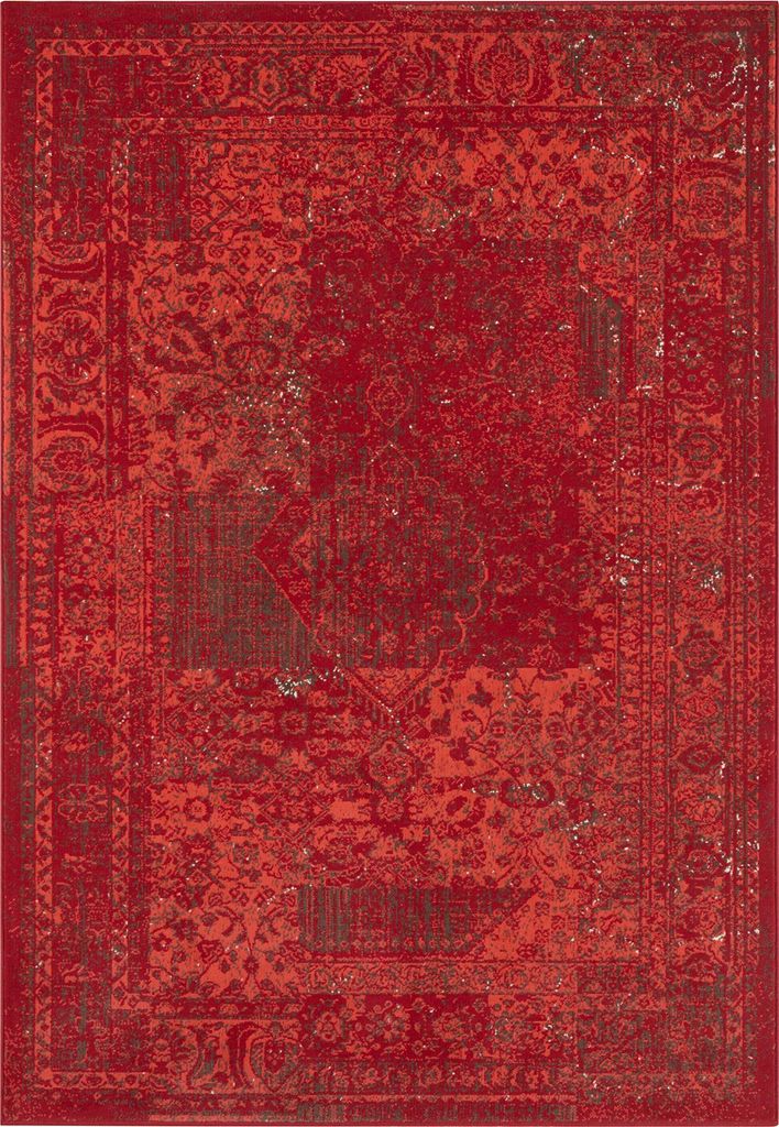 A close-up, top-down view of a red rug with a distressed, vintage-inspired pattern.