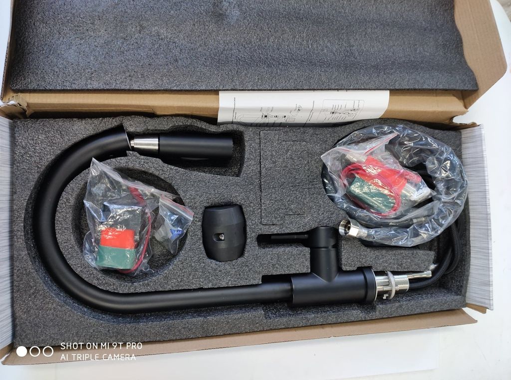 A black kitchen faucet and its accessories are neatly arranged in a cardboard box with foam padding.