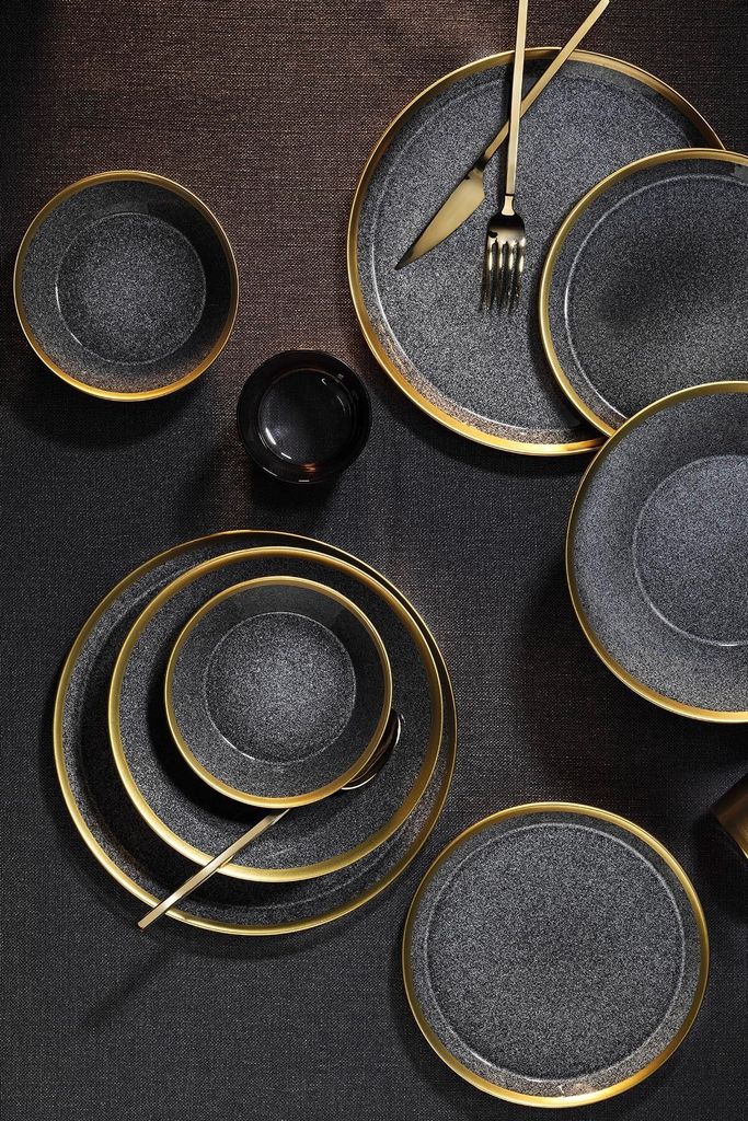 A collection of black and gold rimmed plates and bowls arranged on a dark textured surface.
