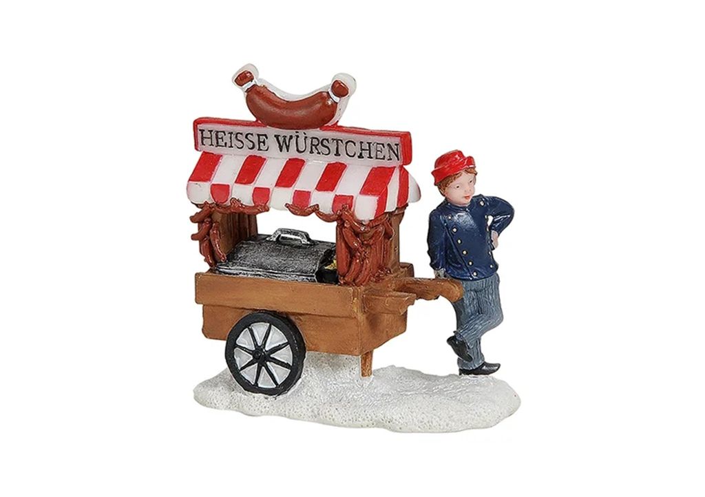 A miniature Christmas village scene featuring a hot dog stand with a vendor.