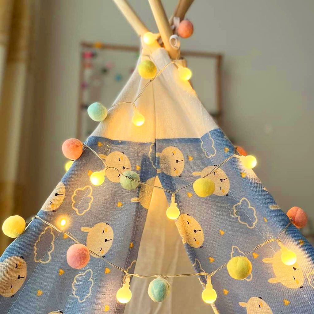 A close-up view of a child's teepee decorated with a string of colorful pom-pom lights.