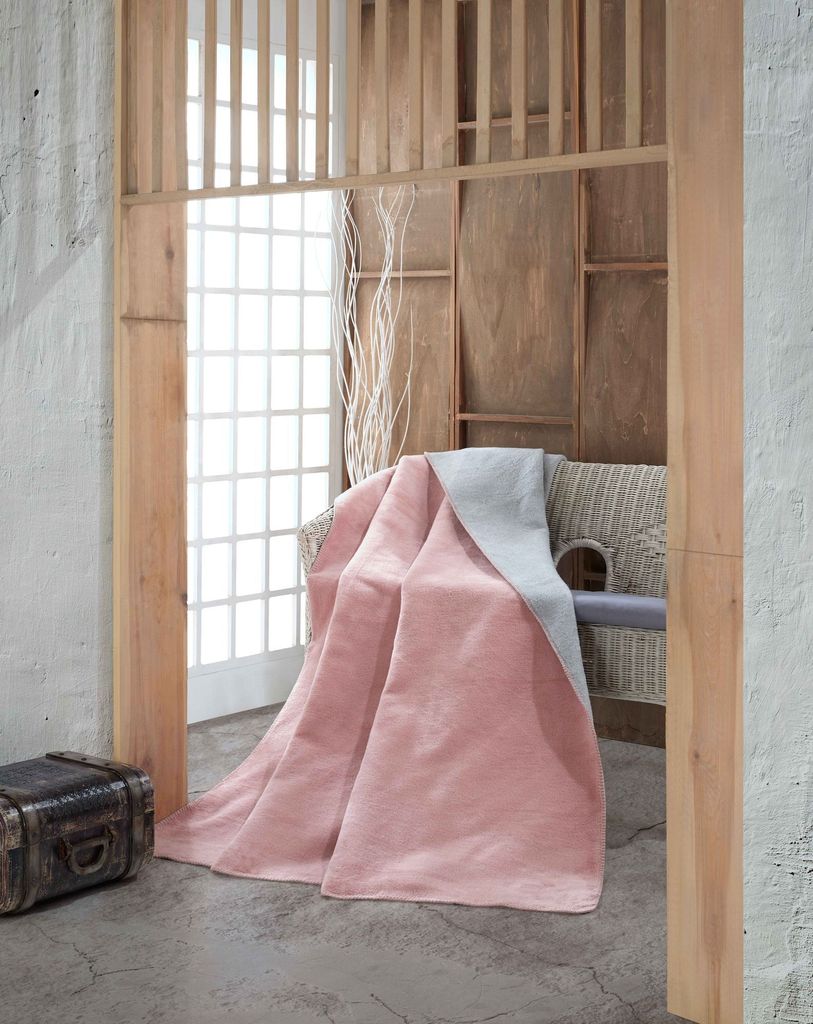 A pink and gray double-faced blanket draped over a chair in a room with wooden accents and a large window.