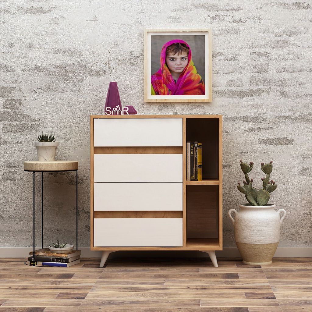 A modern dresser with white drawers and wooden accents, placed against a textured white brick wall. A framed picture of a child wearing a colorful headscarf hangs above it. Decorative items like a vase, books, and a potted cactus are placed around the dres
