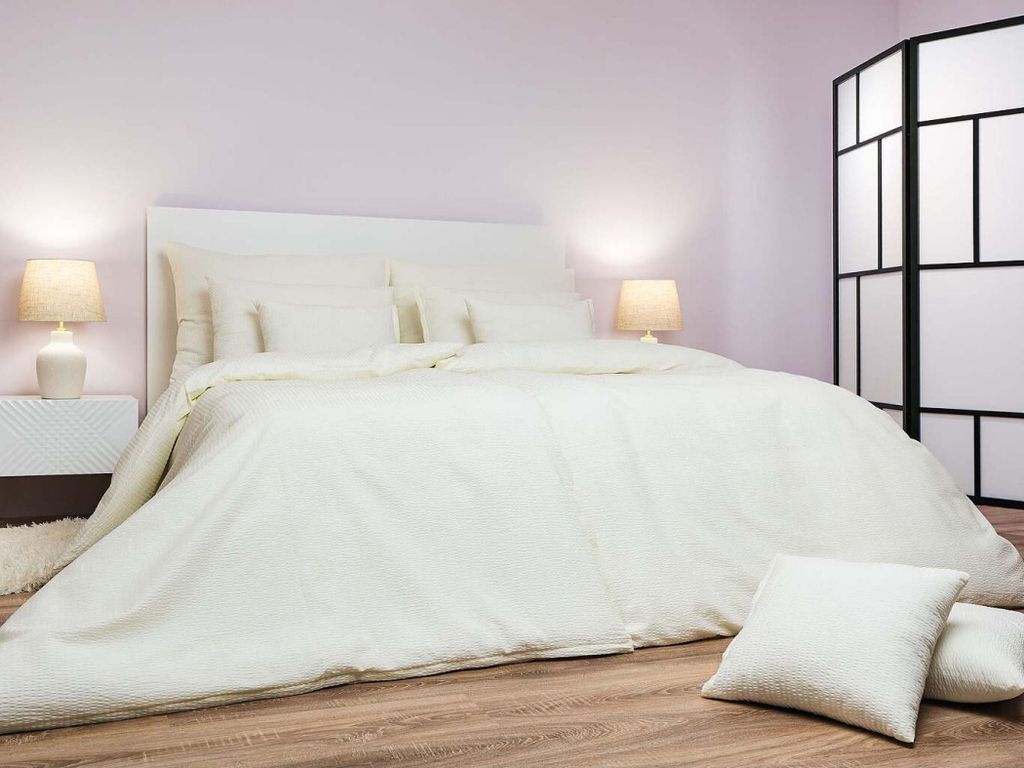 A neatly made bed with white bedding in a room with a light purple wall.