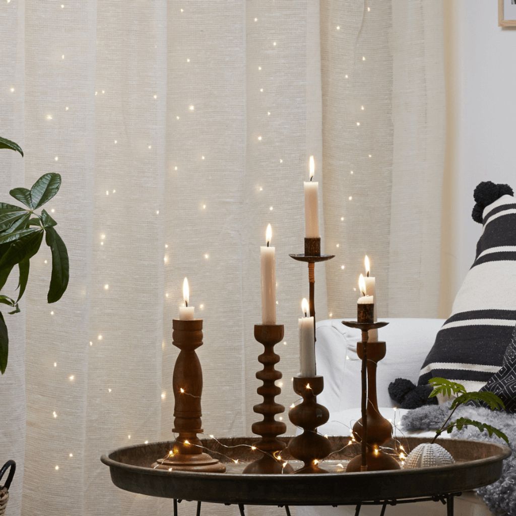 Candles on a tray in front of a curtain with fairy lights.
