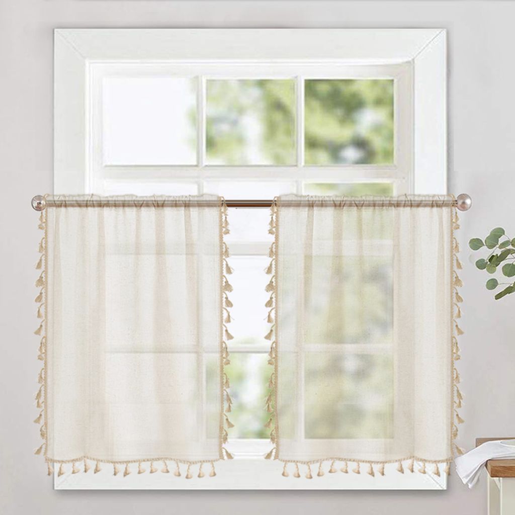 Two sheer curtains with tassels hanging on a window rod in front of a window.