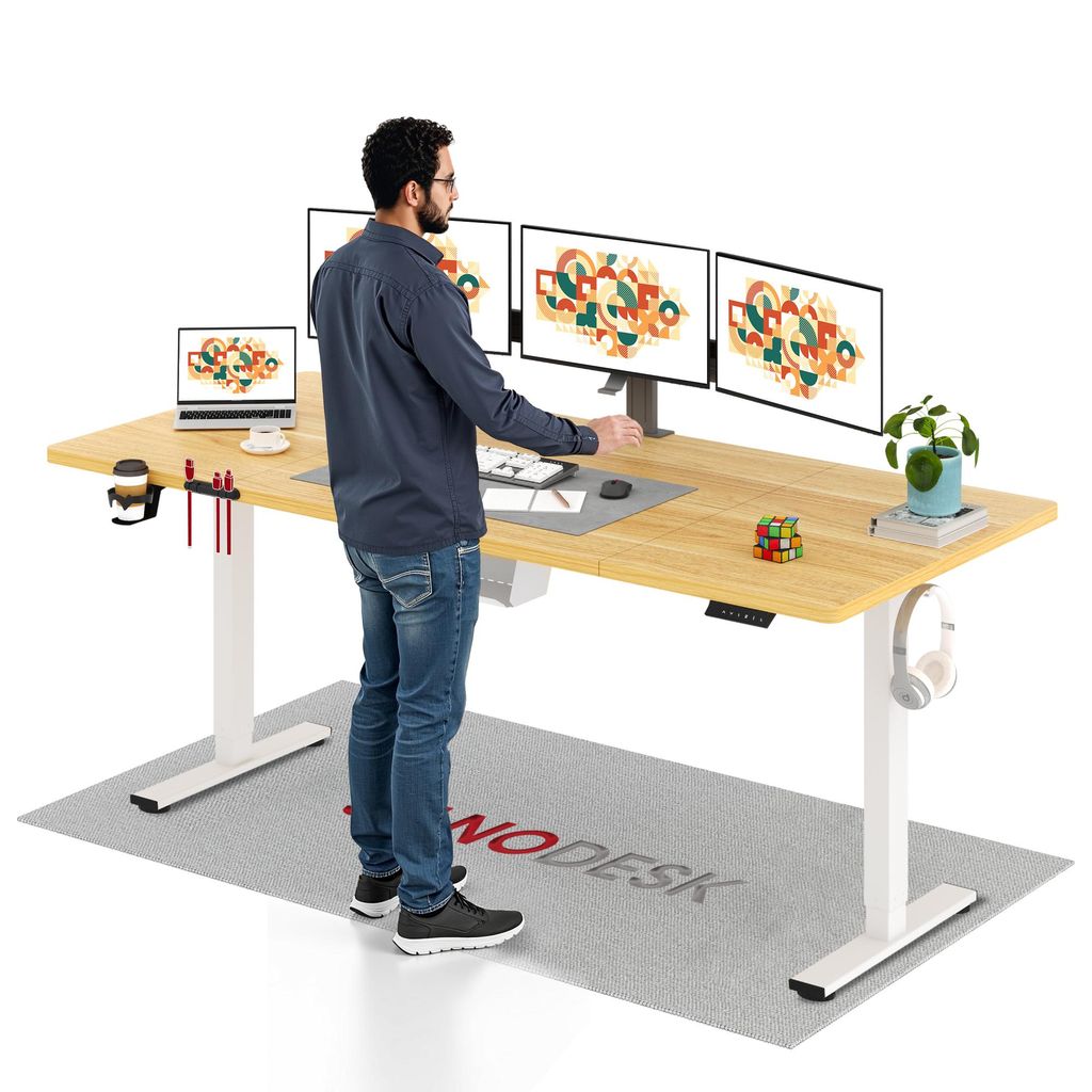 A man is standing at a standing desk with multiple monitors and a laptop.