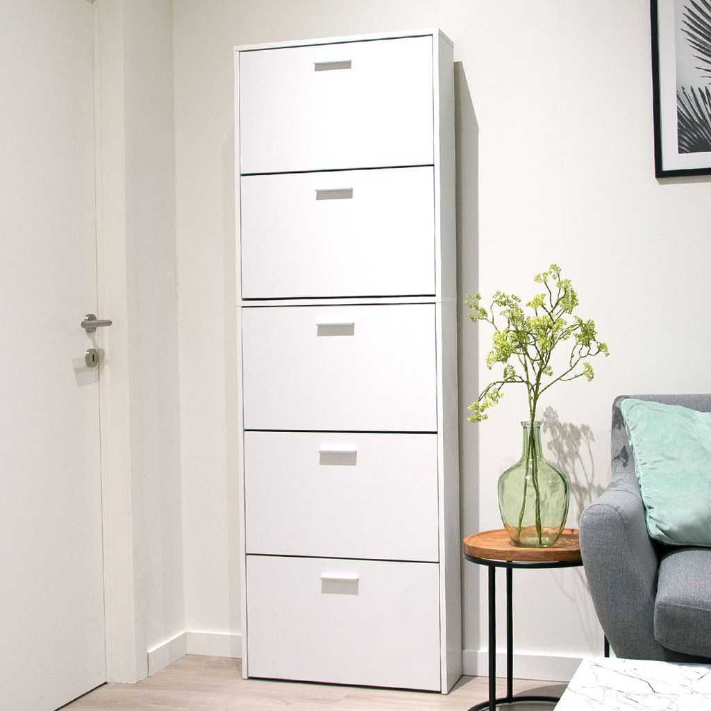 A white shoe cabinet with multiple drawers is shown in a room next to a door and a sofa.