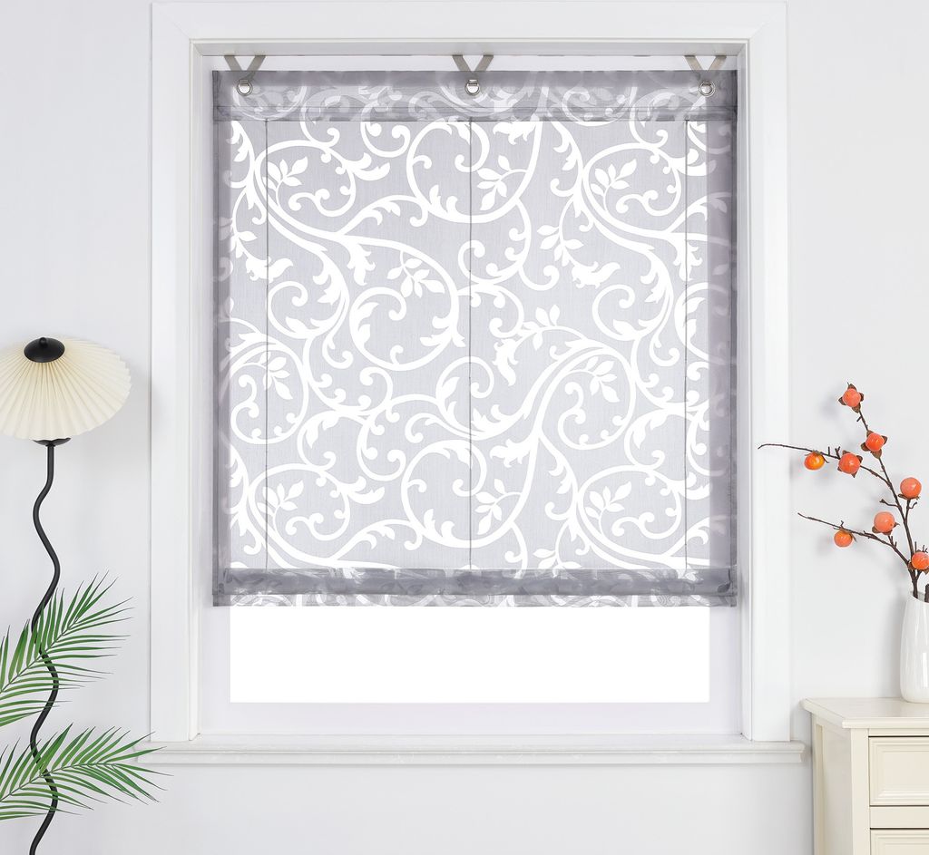 A window with a decorative Roman shade, a floor lamp, and a vase with branches on a nightstand.
