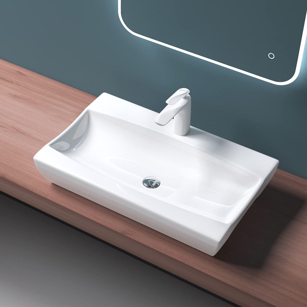A white ceramic sink with a modern faucet sits on a wooden countertop, with a lit mirror in the background.