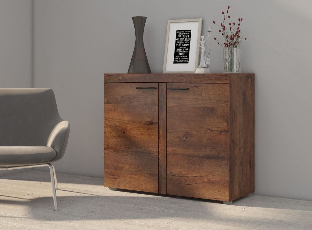 A wooden sideboard with two doors, decorated with a vase and a framed picture, next to a gray armchair.