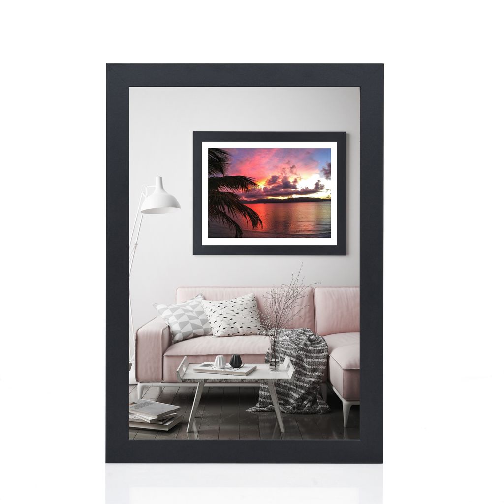 A framed picture of a sunset over the ocean with palm trees in the foreground, displayed in a living room setting with a pink sofa and a coffee table.