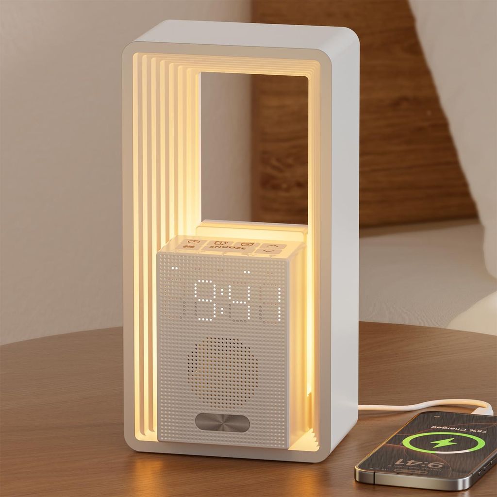 A modern white alarm clock with a digital display and speaker, placed on a wooden surface next to a charging smartphone.