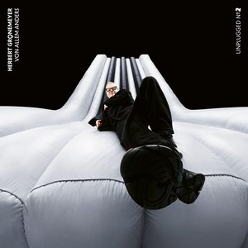 A man in black clothing is lying on a white inflatable structure, with a black background behind him.