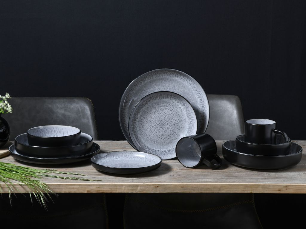 A set of stoneware dishes is arranged on a wooden table against a dark background.