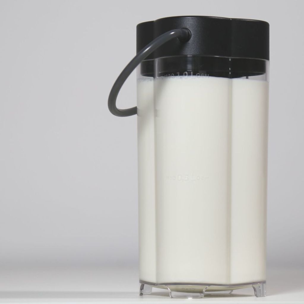 A close-up shot of a milk container with a black lid and handle, filled with white liquid.