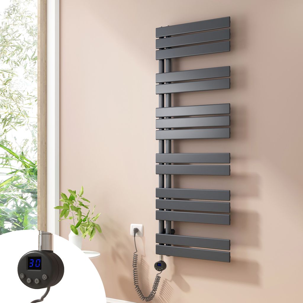 A modern, dark gray electric towel radiator is mounted on a light pink wall next to a window with greenery visible outside. A close-up inset shows the digital controller with temperature display.