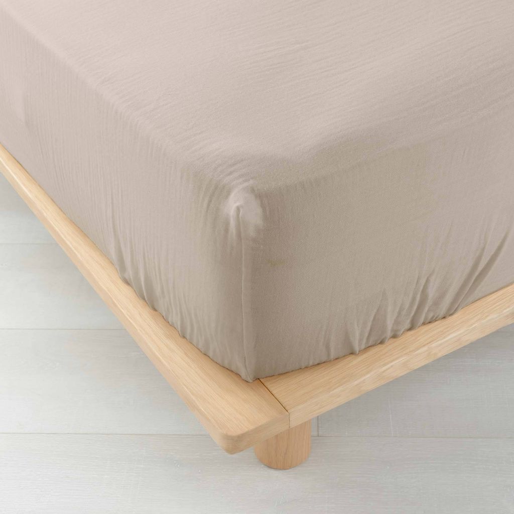 A close-up view of a beige fitted sheet on a wooden bed frame.